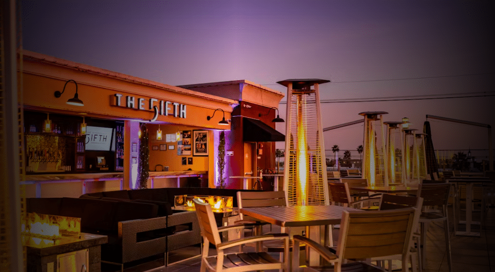 Photo of the Fifth Rooftop Restaurant and Bar with tables and stools, heating lamps visible at twilight.